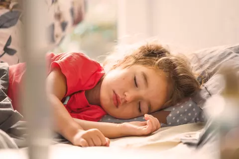 Kleines Kind schläft friedlich im Bett auf einem gepunkteten Kissen.