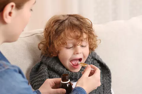 Eine erwachsene Person gibt einem Kind mit einem Löffel Umckaloabo Saft.