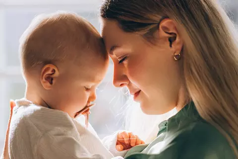 Mutter hält ein Baby im Arm, beide berühren sich zärtlich Stirn an Stirn.