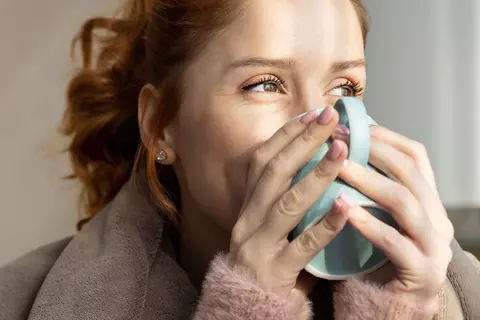 Frau trinkt aus einer großen Tasse und blickt lächelnd