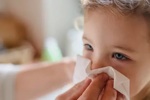 Eine erwachsene Person wischt einem Kind die Nase mit einem Tuch ab.