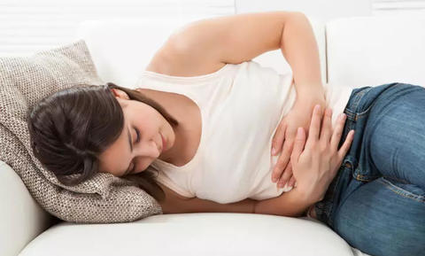 Frau liegt mit Bauchschmerzen auf dem Sofa und hält sich den Bauch