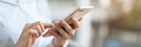 Detailaufnahme der Hände einer jungen Frau die auf ihrem Smartphone tippt