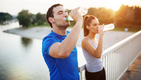 Frau und Mann stehen auf einer Brücke und trinken aus Wasserflaschen