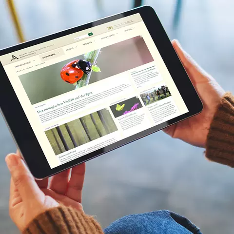 Aufsicht auf ein Tablet mit der Website der Akademie für Natur- und Umweltschutz Baden-Württemberg, dass eine junge Frau in den Händen hält