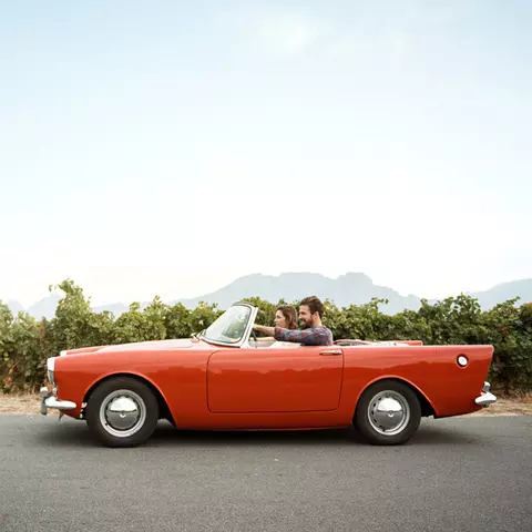Ein junges Paar in einem roten Sport-Cabrio in südlicher Landschaft