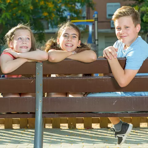 Lachende Kinder, die sich auf die Lehne einer Parkbank stützen