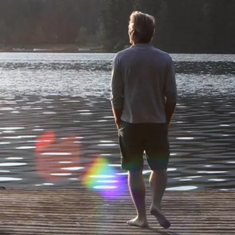 Ein Mann von hinten der an einem See auf einem Holzsteg steht