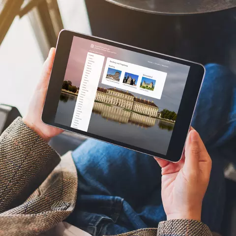 Aufsicht auf ein Tablet mit geöffneter Website des virtuellen Museums-Angebots der Bayrischen Schlösserverwaltung, dass eine junge Frau in den Händen hält