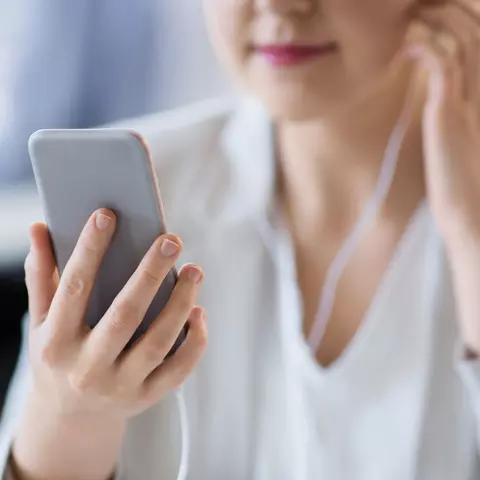 Eine junge Frau hört mit einem Kopfhörer einen Podcast auf Ihrem Smartphone