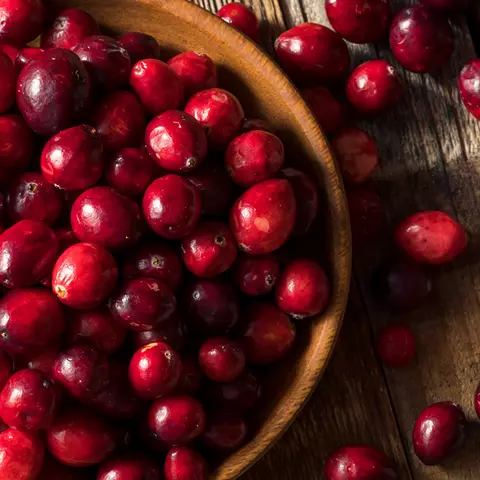 Cranberries in einer Schale, die auf einer Holzplatte steht. Weitere Cranberries sind um die Schale verteilt