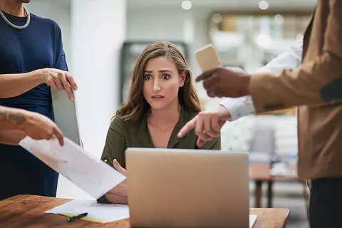 Junge Frau am Arbeitsplatz ist gestresst durch auf sie einredende Kollegen